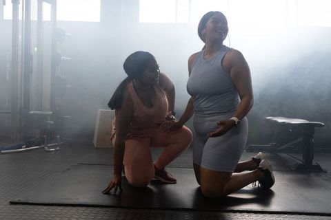 African american women kneeling on mat celebrating workout in backlit gym studio