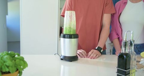 Couple blending vibrant green smoothie on modern kitchen island with fresh basil