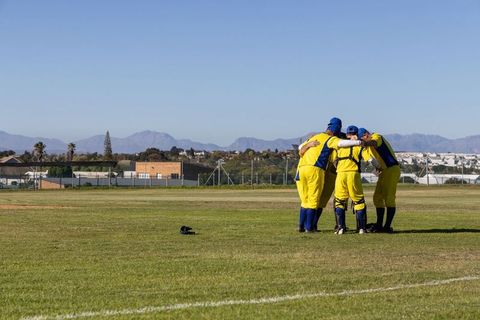 Yellow-and-blue cricket team huddling on sunny field with mountain vista
