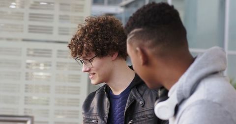 Two male students chatting on campus, casual conversation with leather jacket and headphones