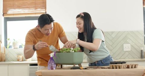 Couple repotting seedlings on kitchen counter with green planter trowel and potting soil