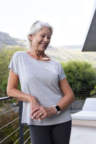 Senior woman wearing smartwatch and ring standing on sunlit terrace overlooking green hills