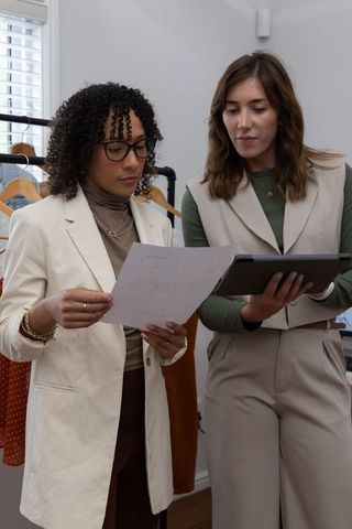Diverse female coworkers collaborating over design sketches and tablet in fashion showroom