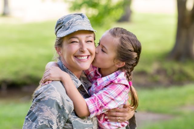 Happy female soldier being kissed by her daughter in park on sunny day