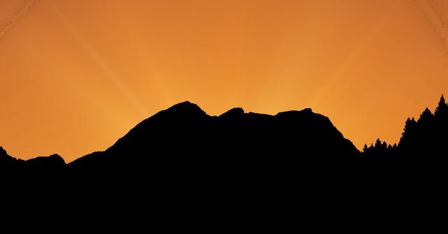 Silhouette of a mountain range against a vibrant orange sunset sky. Ideal for use in travel brochures, nature-themed websites, inspirational posters, and backgrounds for presentations. The dramatic contrast between the dark mountains and the bright sky creates a striking visual effect, perfect for conveying themes of tranquility, adventure, and natural beauty.