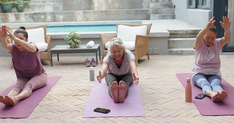 Diverse senior women practicing seated mat stretches poolside for fitness and wellbeing