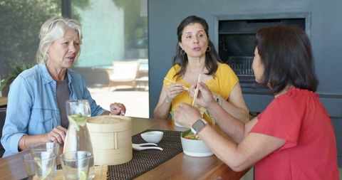 Three women sharing relaxed lunch and conversation with dim sum, chopsticks, lemon water