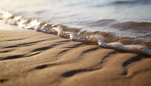 Sunrise wave lapping rippled golden sand with sparkling reflections and coastal texture