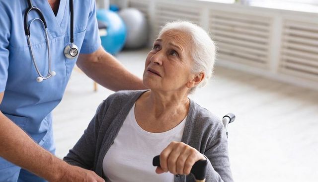 Senior woman gripping walker while nurse assisting mobility during rehabilitation session