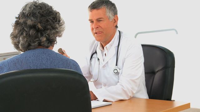 Senior male doctor is conversing with a mature female patient in a clinical setting. This image captures a healthcare consultation, showcasing compassion and professional care. Ideal for use in healthcare brochures, patient care articles, or medical service websites, emphasizing doctor-patient communication and trust in medical settings.