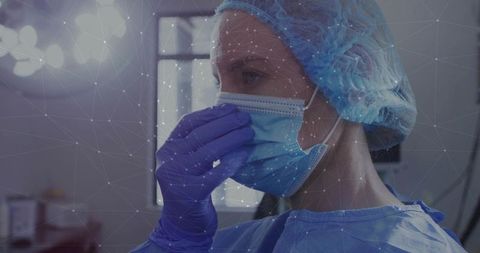 Medical worker adjusting surgical mask while wearing gown, bouffant cap and gloves in or