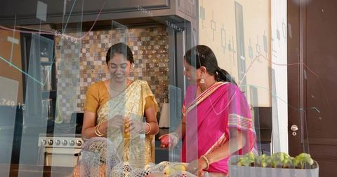 Indian women in colorful saris peeling fruit at modern kitchen counter with double exposure