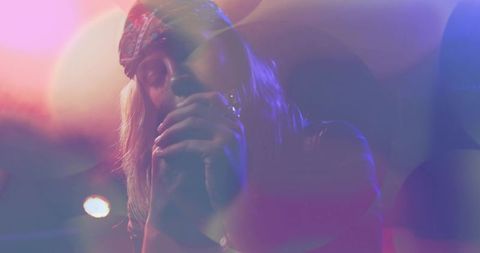 Moody neon concert singer cupping microphone under bandana, backlit haze and lensflare