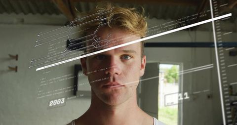 Young man in industrial workshop with transparent code overlays and digital schematic
