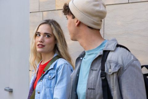 Young couple walking and talking along light stone wall woman turning to look at partner
