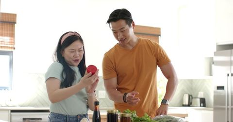 Asian couple reading jar label while preparing meal in bright modern kitchen together