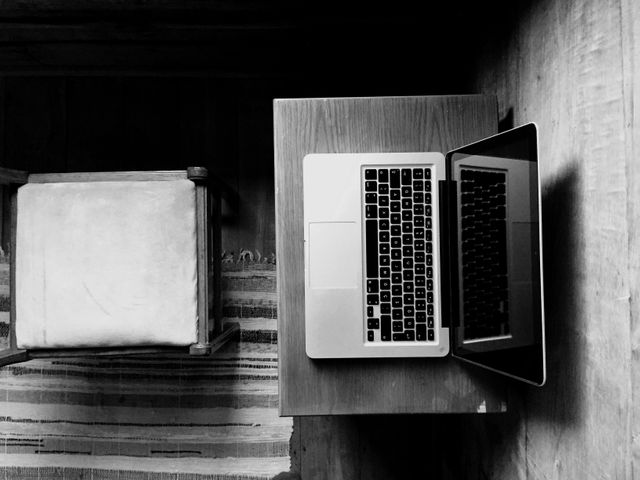 This image captures a minimalist home office setup with a laptop and a wooden chair from a top-down perspective in a monochromatic style. Ideal for illustrating remote work, home office environments, technology, and minimalist lifestyle articles.