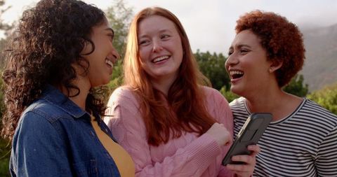 Diverse Female Friends Laughing Together Holding Smartphone