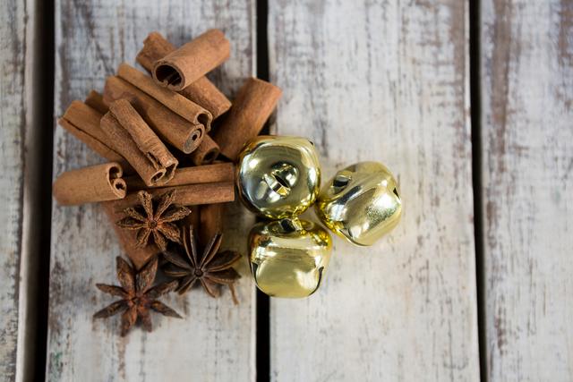 Cinnamon sticks, star anise, and golden bells arranged on a rustic wooden plank. Perfect for holiday-themed projects, Christmas decorations, seasonal recipes, and festive marketing materials. Ideal for evoking a cozy and warm holiday atmosphere.