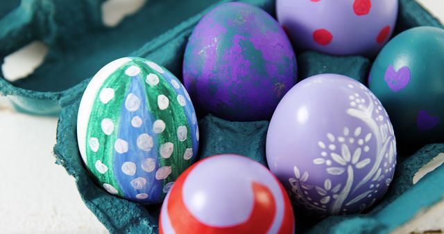 Vibrantly hand-painted Easter eggs with various patterns including polka dots, floral motifs, and abstract designs resting in blue carton. Ideal for use in holiday cards, festive decoration ideas, DIY craft guides, and articles related to spring or Easter celebrations.