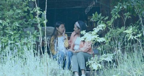 Mother comforting daughter on overgrown porch steps during heartfelt garden conversation