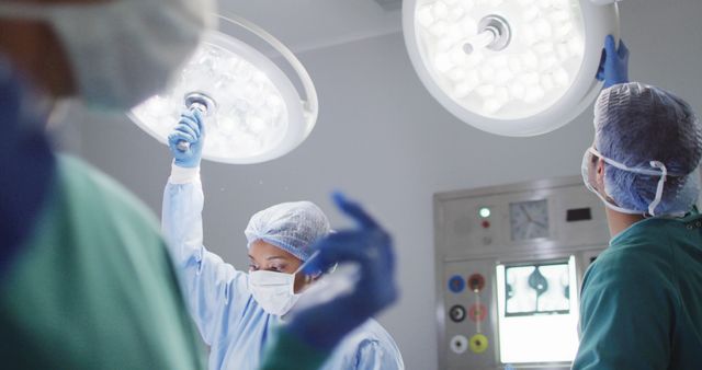 Surgical team preparing for a procedure in a well-equipped operating room, adjusting sterile lights while wearing protective gear like gloves, masks, and surgical gowns. Perfect for illustrating medical and healthcare themes, hospital environments, surgical procedures, teamwork and clinical settings.