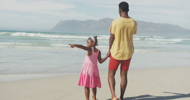 African american father and daughter holding hands walking at the beach. family travel and vacation concept
