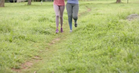 Companions walking side-by-side on grassy park trail wearing leggings and sneakers