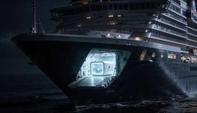 Cruise ship bow revealing illuminated modular medical unit on open sea night, emergency ramp
