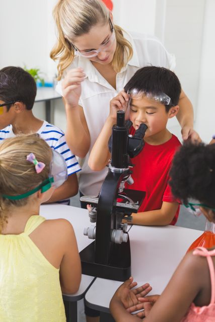 Teacher helping children use a microscope in a school laboratory. Ideal for educational content, science programs, school brochures, and STEM learning materials.