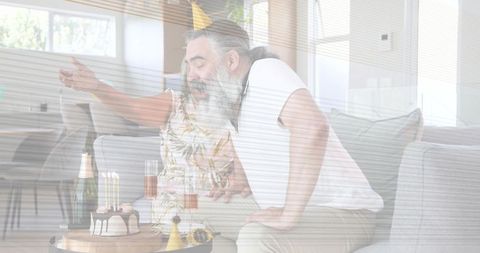 Senior Couple Celebrating Birthday at Home Blowing Candles on Cake with Champagne