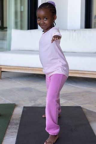 African american girl practicing yoga balance on patio wearing pink sweatpants barefoot