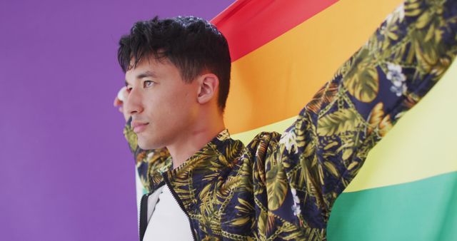 Young person holding a rainbow flag, symbolizing LGBTQ pride and diversity. The vibrant purple background adds a pop of color and emphasizes the flag's importance. This image is ideal for use in materials promoting LGBTQ events, pride celebrations, or campaigns focused on equality and diversity.