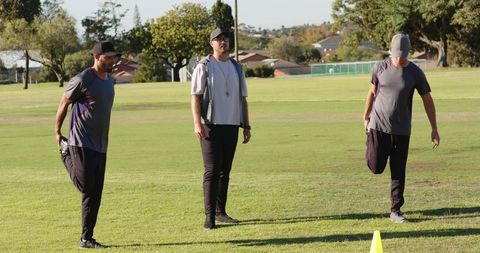 Coach leading outdoor warm-up: athletes performing quad stretches and lateral bends