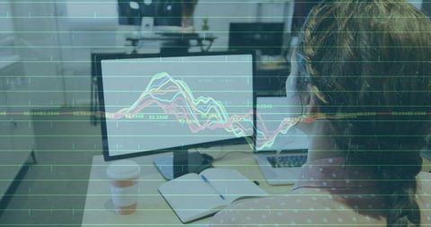 Analyst studying stock charts on office monitor with notebook and coffee