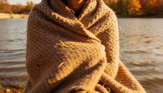 Cozy knit blanket wrapping person by autumn lake at golden hour