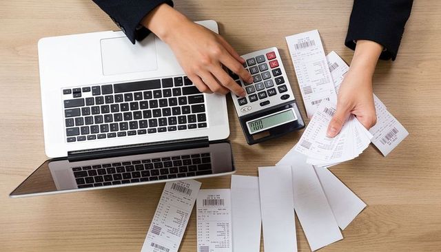 Counting receipts with calculator and laptop for expense tracking and budgeting