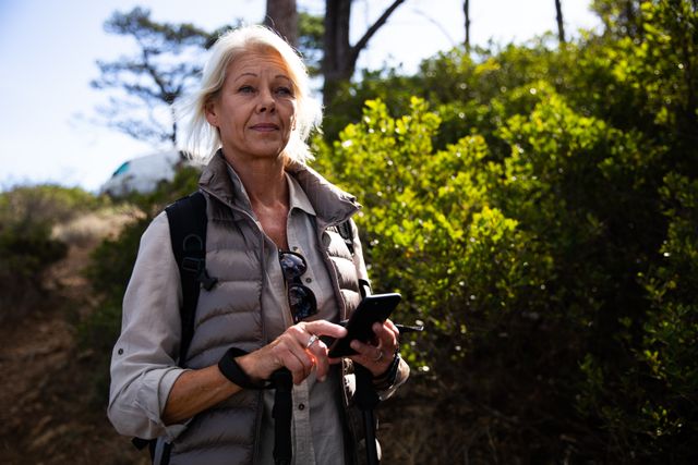 Front view portrait of a senior Caucasian woman enjoying her time in nature, walking in the woods, using a smartphone
