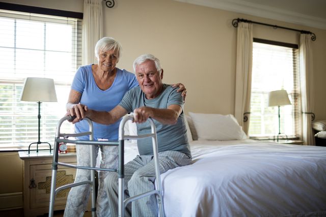 Senior woman helping elderly man use a walker in a cozy bedroom. Ideal for topics on elderly care, mobility assistance, aging, family support, and home healthcare. Can be used in articles, blogs, and advertisements related to senior living, caregiving, and health services.