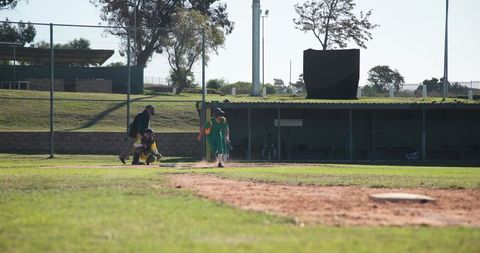 Baseball batter sprinting to home plate with catcher and umpire on grassy field