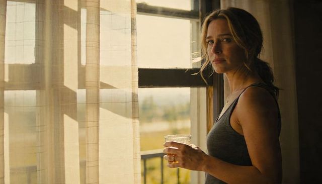 Contemplative woman standing at balcony window holding glass during golden hour