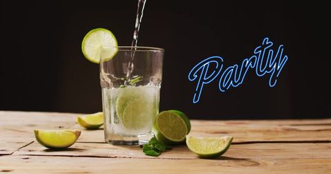 Glass of cocktail filled with fresh lime slices and mint on wooden table, illuminated by vibrant neon party sign against black background. Perfect for themes of nightlife, celebrations, events promotion, summer gatherings, or beverage marketing material, conveying atmosphere of celebration and refreshment.