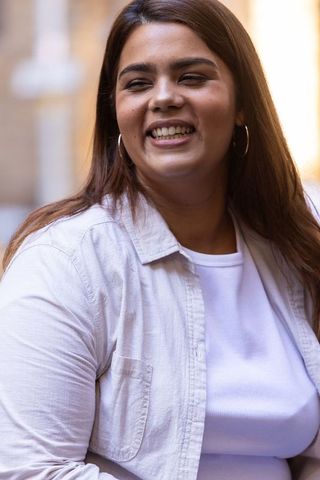 Sunlit african woman smiling in urban courtyard wearing white top and beige overshirt