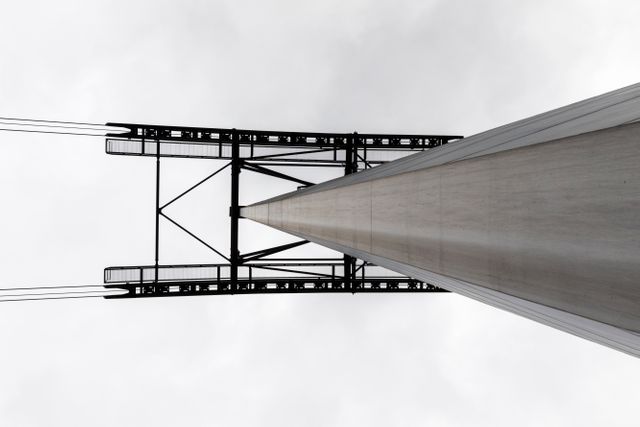 This image captures an upward view of a ski lift tower with a cloudy sky as the backdrop, highlighting the steel framework and cables. Useful for websites on ski resorts, infrastructure, engineering marvels, and minimalist perspectives.