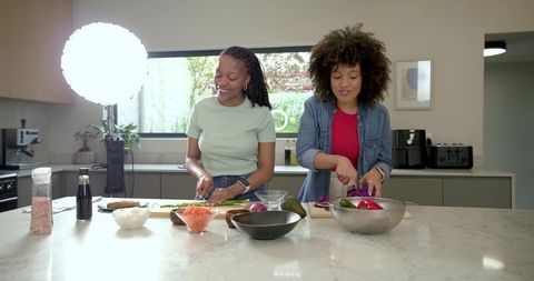 Two diverse women chopping vegetables on marble kitchen island during relaxed meal-prep