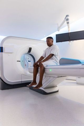African american man sitting on mri scanner table in bright modern diagnostic room