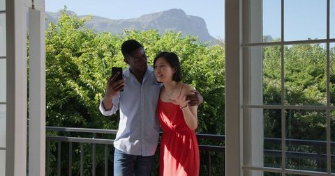 Happy Couple Taking Selfie on Sunlit Balcony embracing Nature