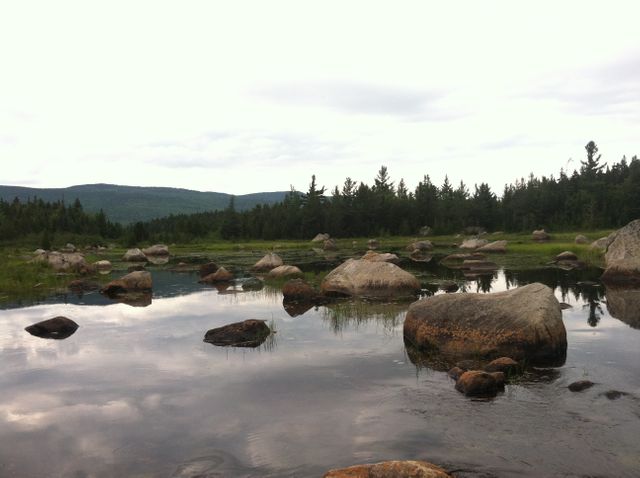 This image can be used to evoke a sense of tranquility and connection with nature. Ideal for websites or advertisements related to camping, hiking, outdoor adventures, or wellness retreats. The serene mountain lake setting with large boulders reflects calm waters and invites viewers to imagine a peaceful escape.