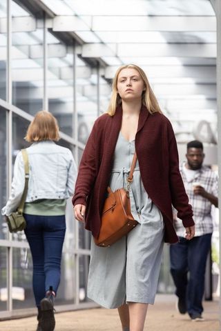 Urban skybridge pedestrians walking past mirrored glass woman in maroon cardigan carrying tan bag