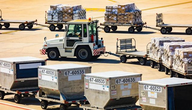 Airport ground tractor towing cargo dollies and uld containers across sunlit apron